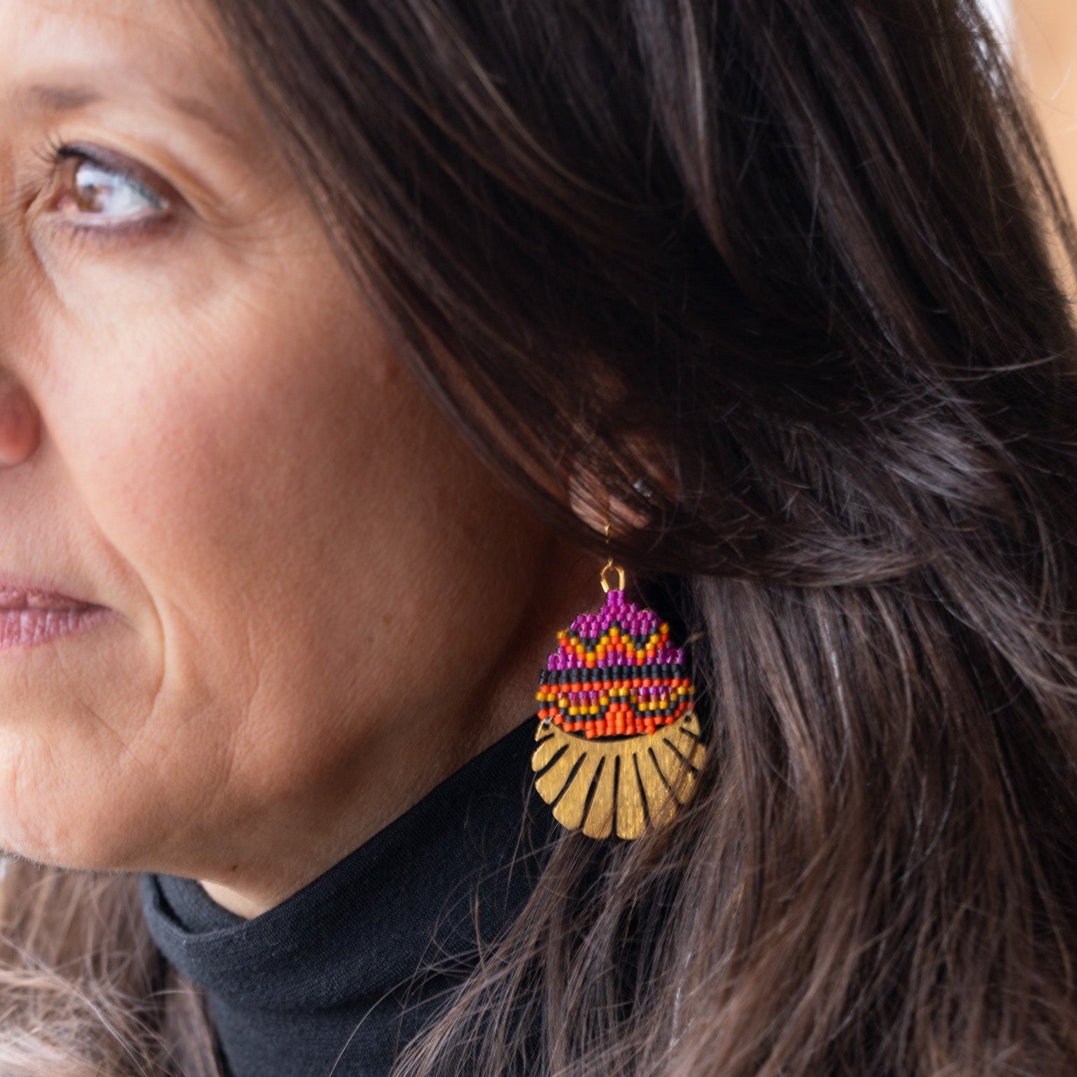Close-up of a woman wearing colorful beaded earrings with a neutral background