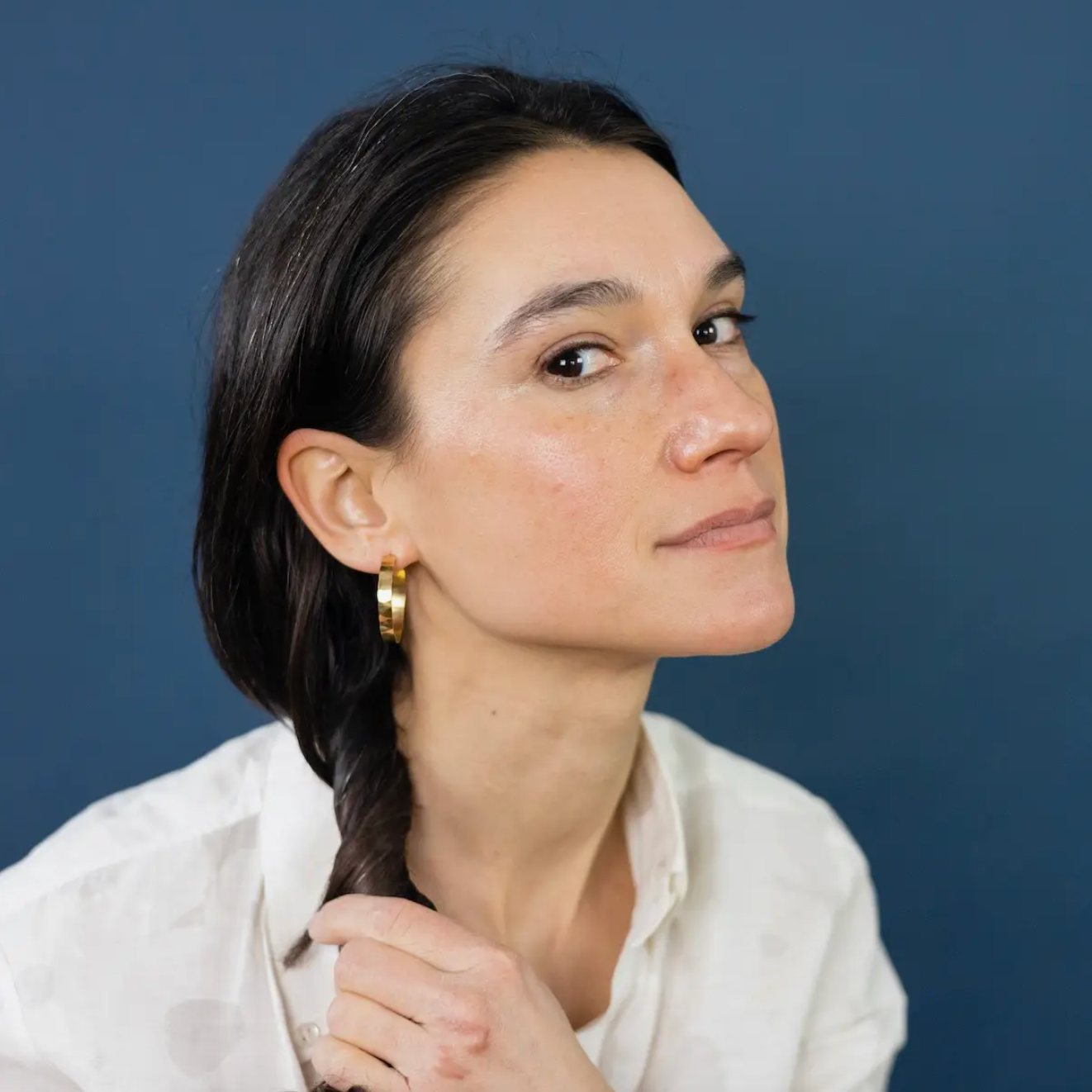 Woman wearing large thin gold hammered hoops, side view.