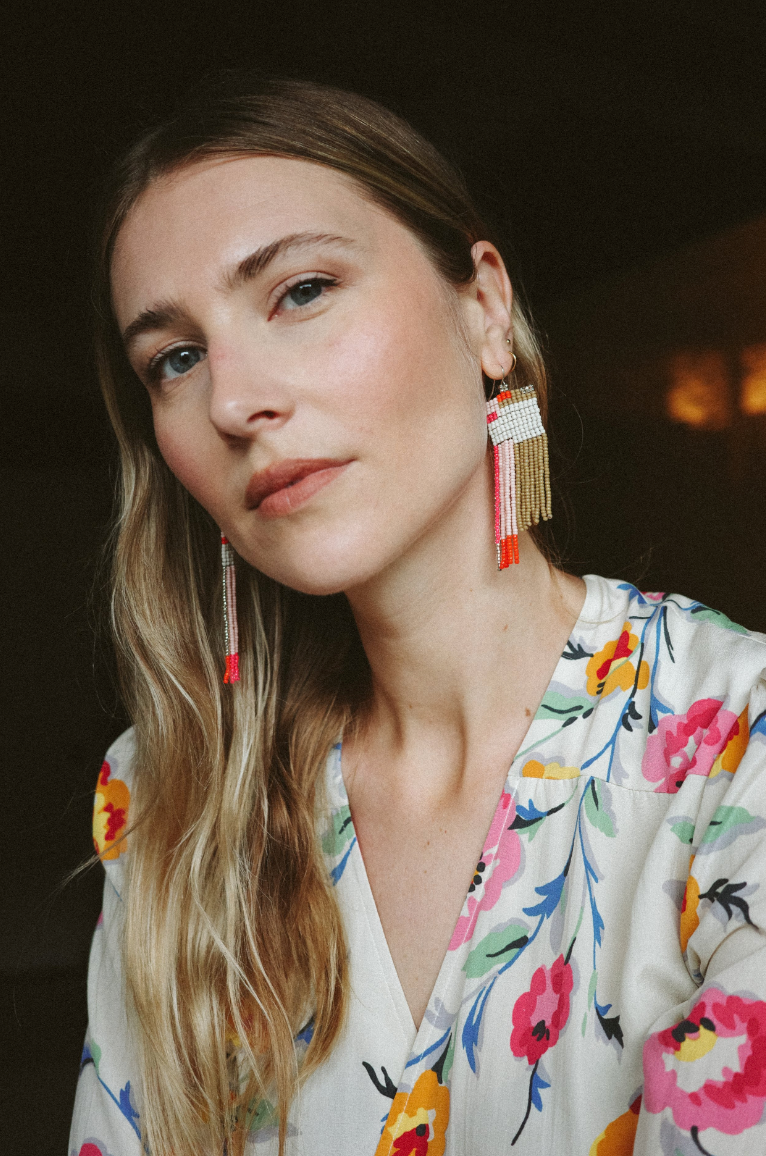 Woman wearing white, pink, orange, brown hand beaded earrings.