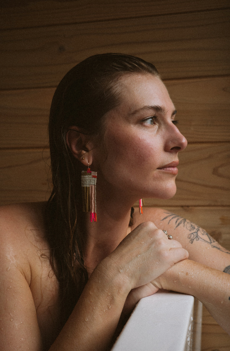 Woman wearing white, pink, orange, brown hand beaded earrings, side view.