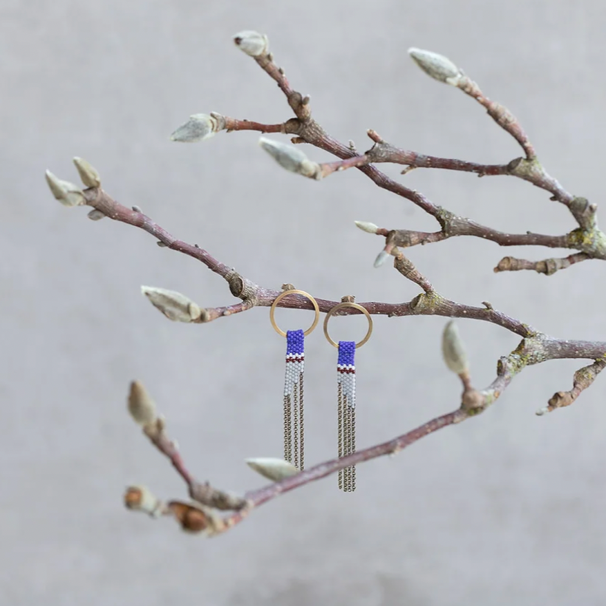 Hand beaded earrings made of gold stud rings wit blue and gray beaded chain, hanging from branches.