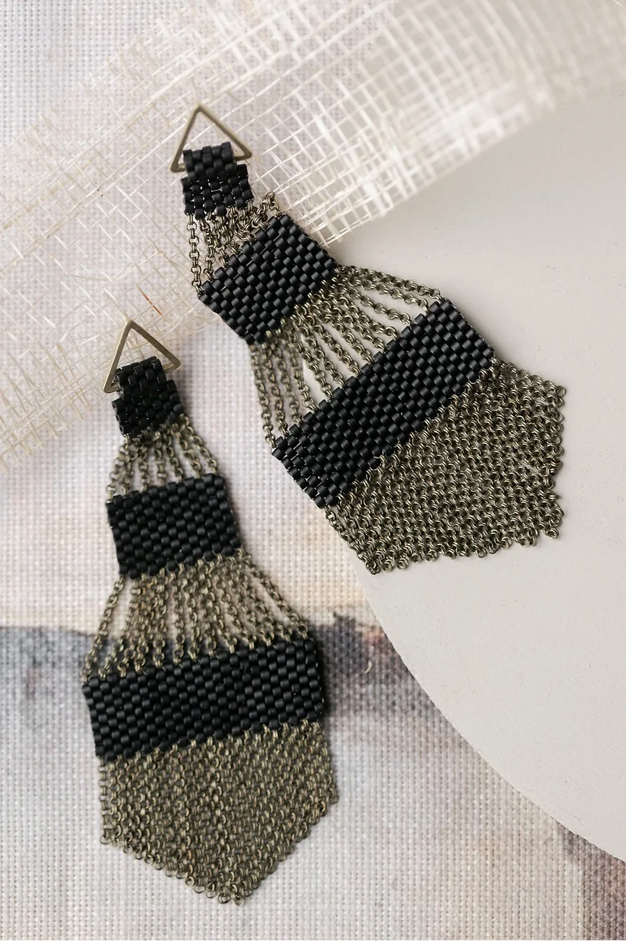 Pair of large black beaded chandelier shaped earrings on a light background.