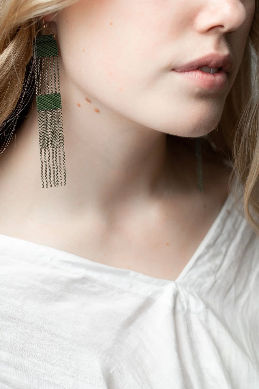 Woman wearing long dangle earrings made from moss greeen beads and brass chains.