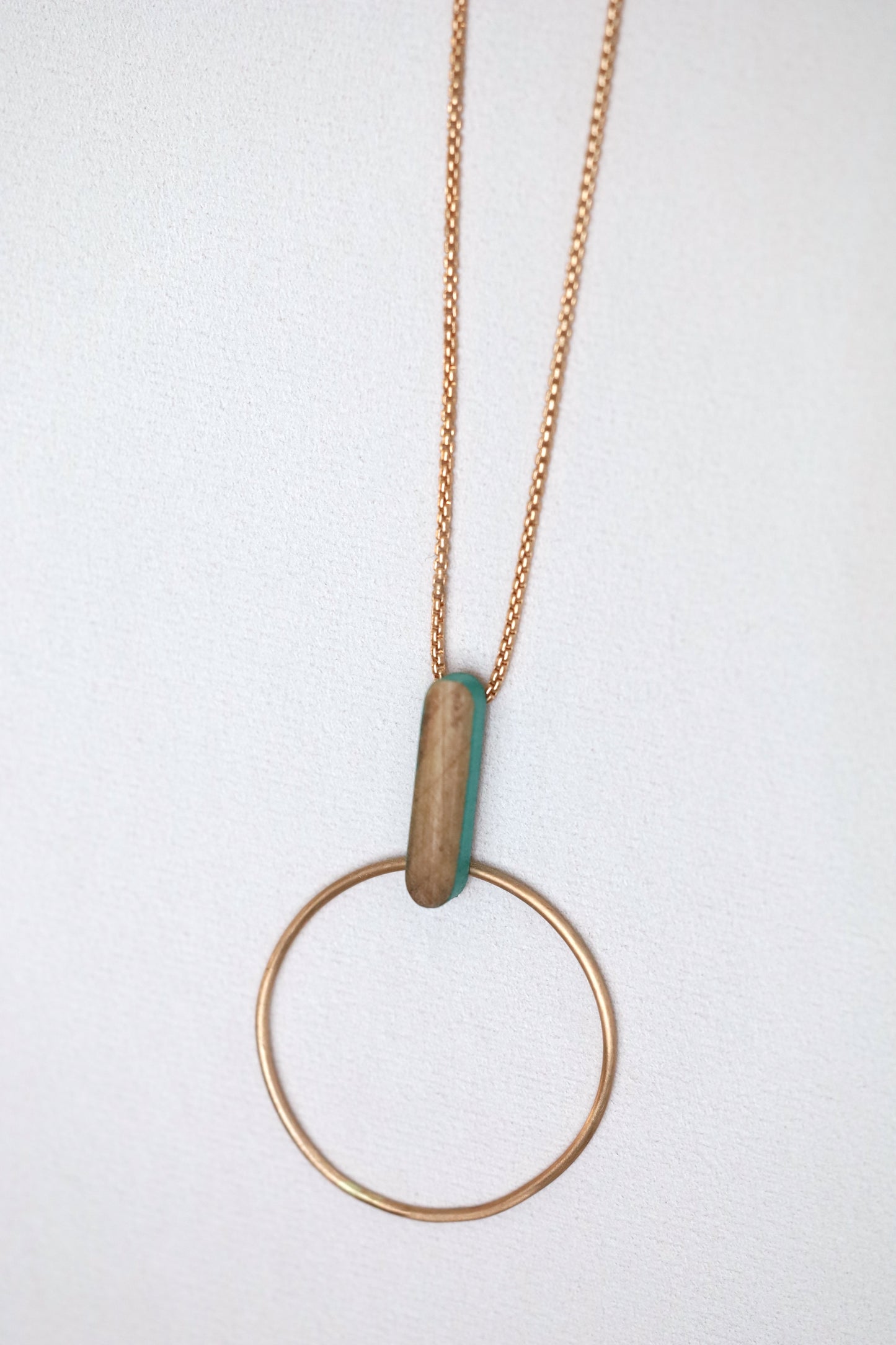 Bronze circle and wooden dash pendant suspended from bronze chain necklace, on a light background.