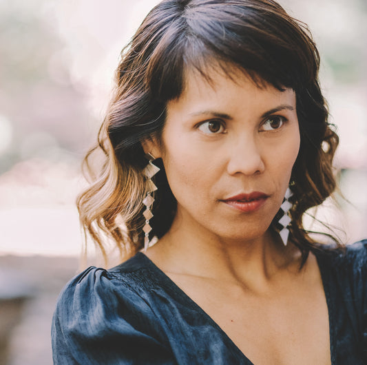 Woman wearing long silver earrings made from diamond shapes that hang straight down.