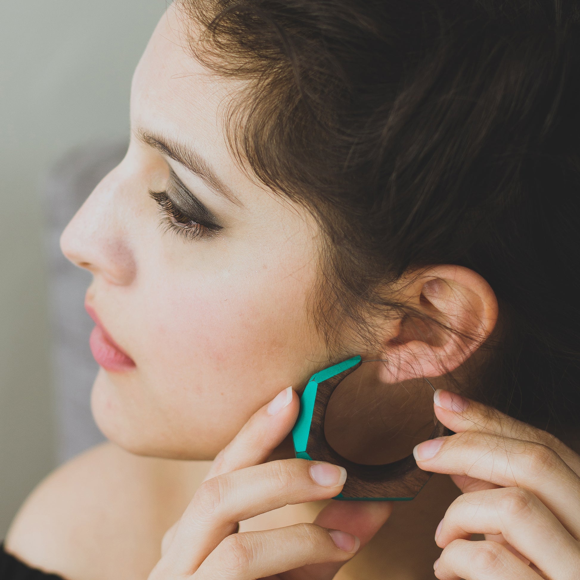 Woman putting on large statement hoop earrings made from wood with turquoise painted accents.