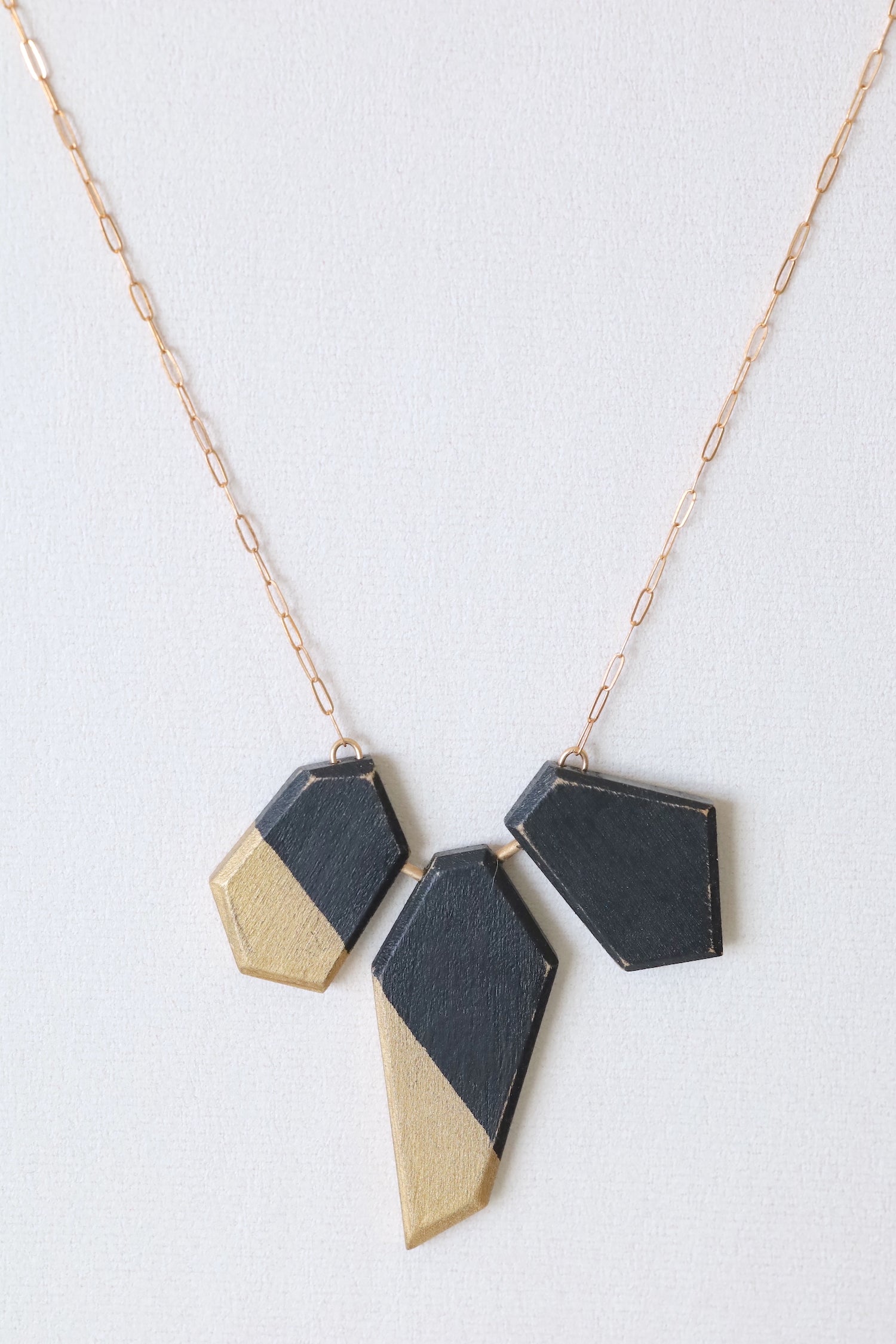 Wooden pieces painted black and gold on a bronze chain. Straight on view.