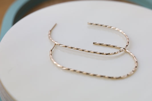 Pair of large twisted gold hoop earrings. Close up.