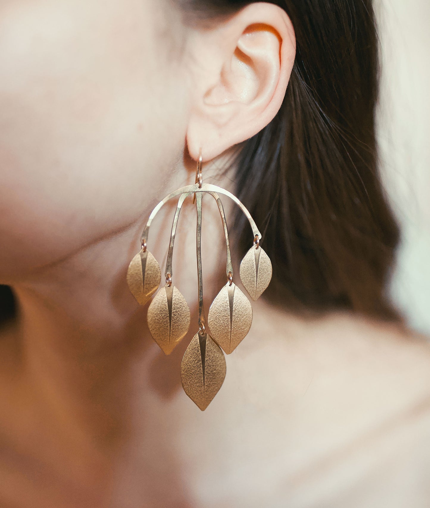 Close up of woman wearing large gold statement earrings made from leaf shapes.