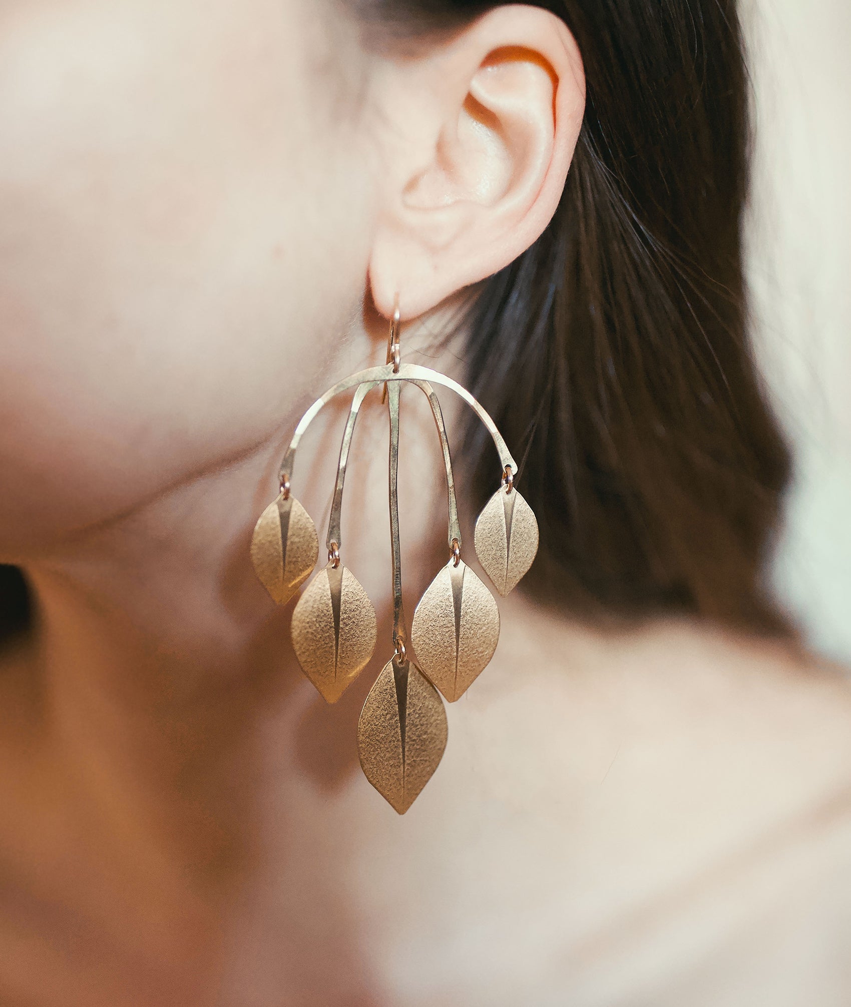 Close up of woman wearing large gold statement earrings made from leaf shapes.