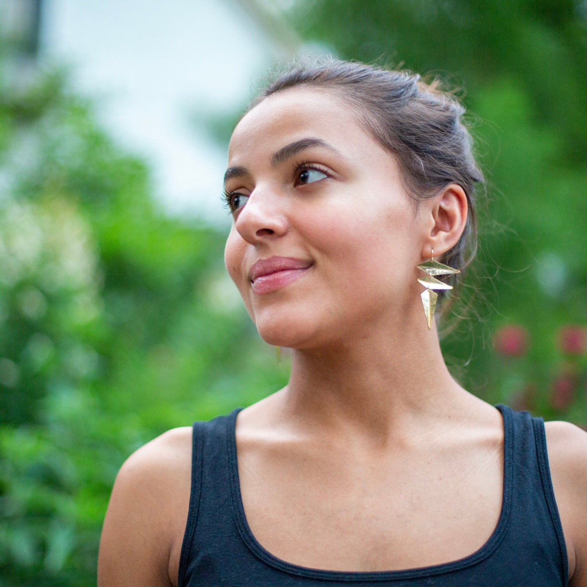 Woman wearing gold earrings made from angular hammered metal shapes, side view.