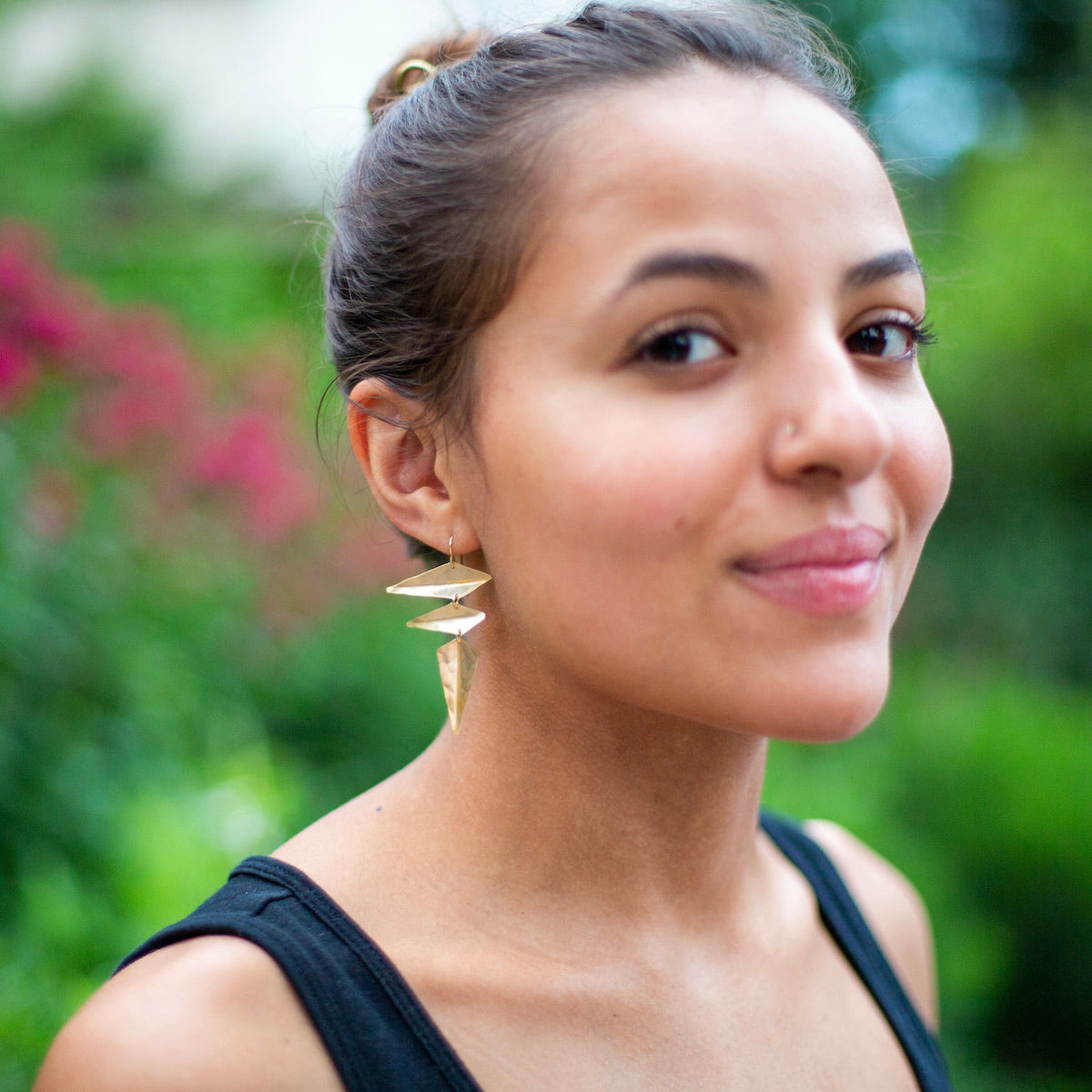 Woman wearing gold earrings made from angular hammered metal shapes.