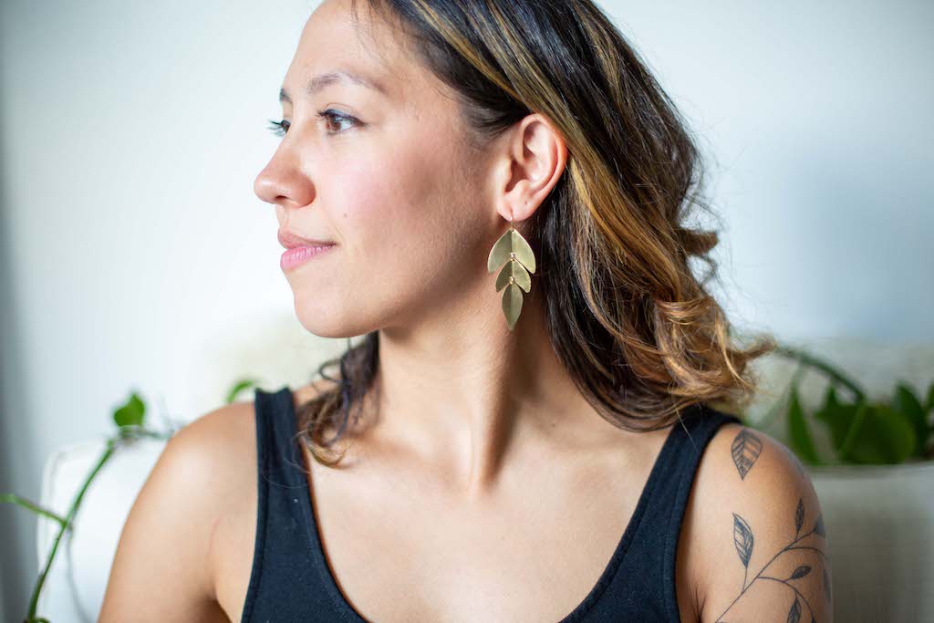 Woman wearing gold leaf shaped dangle earrings made from hammered metal.