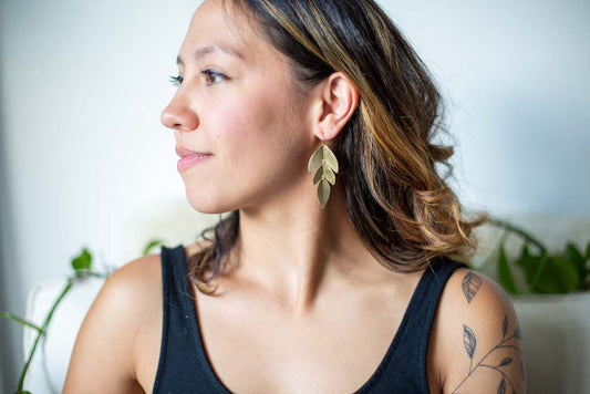 Woman wearing gold leaf shaped dangle earrings made from hammered metal.