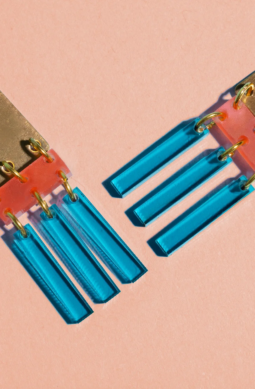 Close up of brass and colorful acrylic earrings with teal fringe.