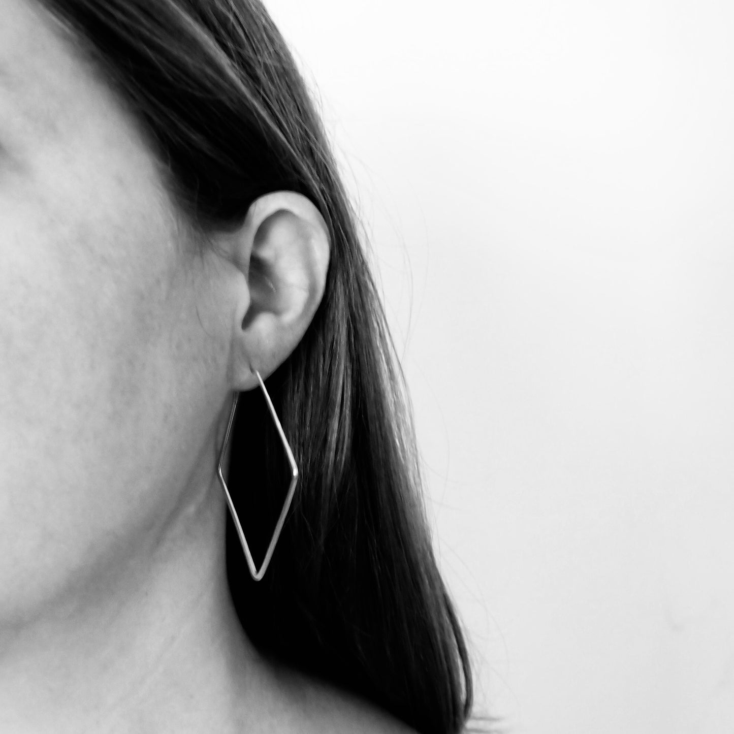 Woman wearing diamond shaped hoop earrings.