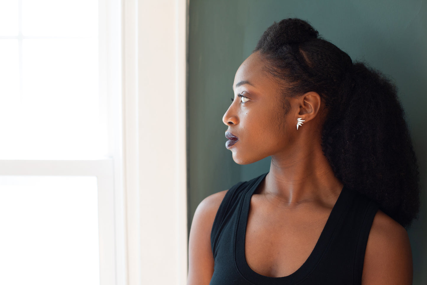 Woman wearing spiky stud earrings looking toward window.