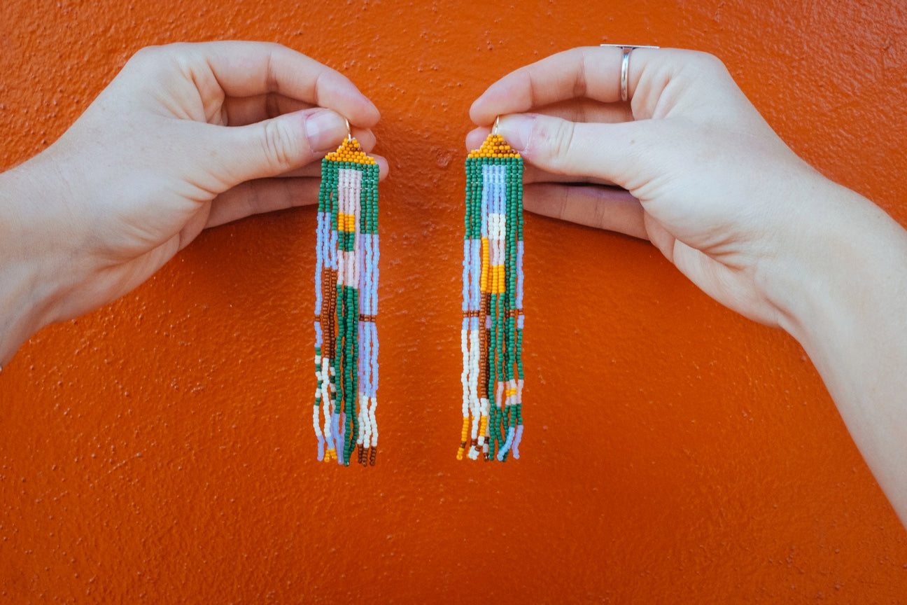 Person holding up colorful beaded earrings in green, gold, blue and red.