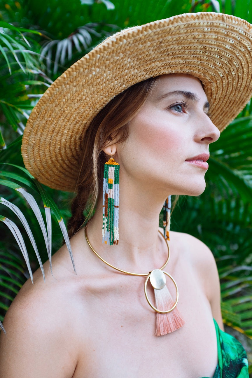 Woman wearing long colorful beaded earrings in green, gold, blue and red.