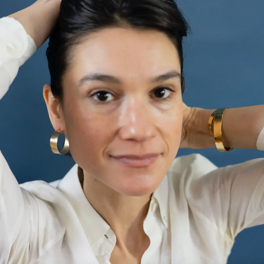 Front view of woman wearing large, flat hammered gold hoop earrings.
