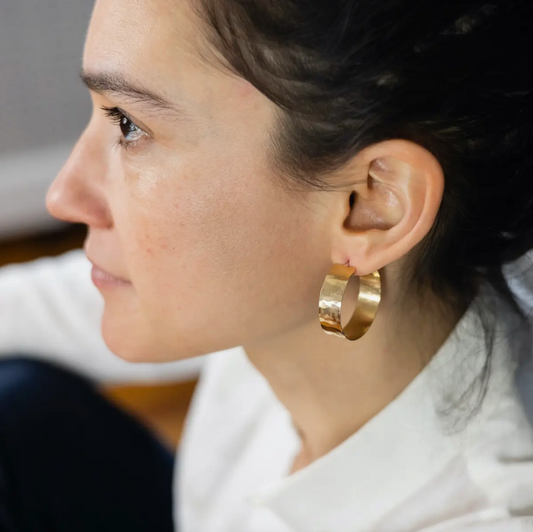 Side view of woman wearing large, flat hammered gold hoop earrings.