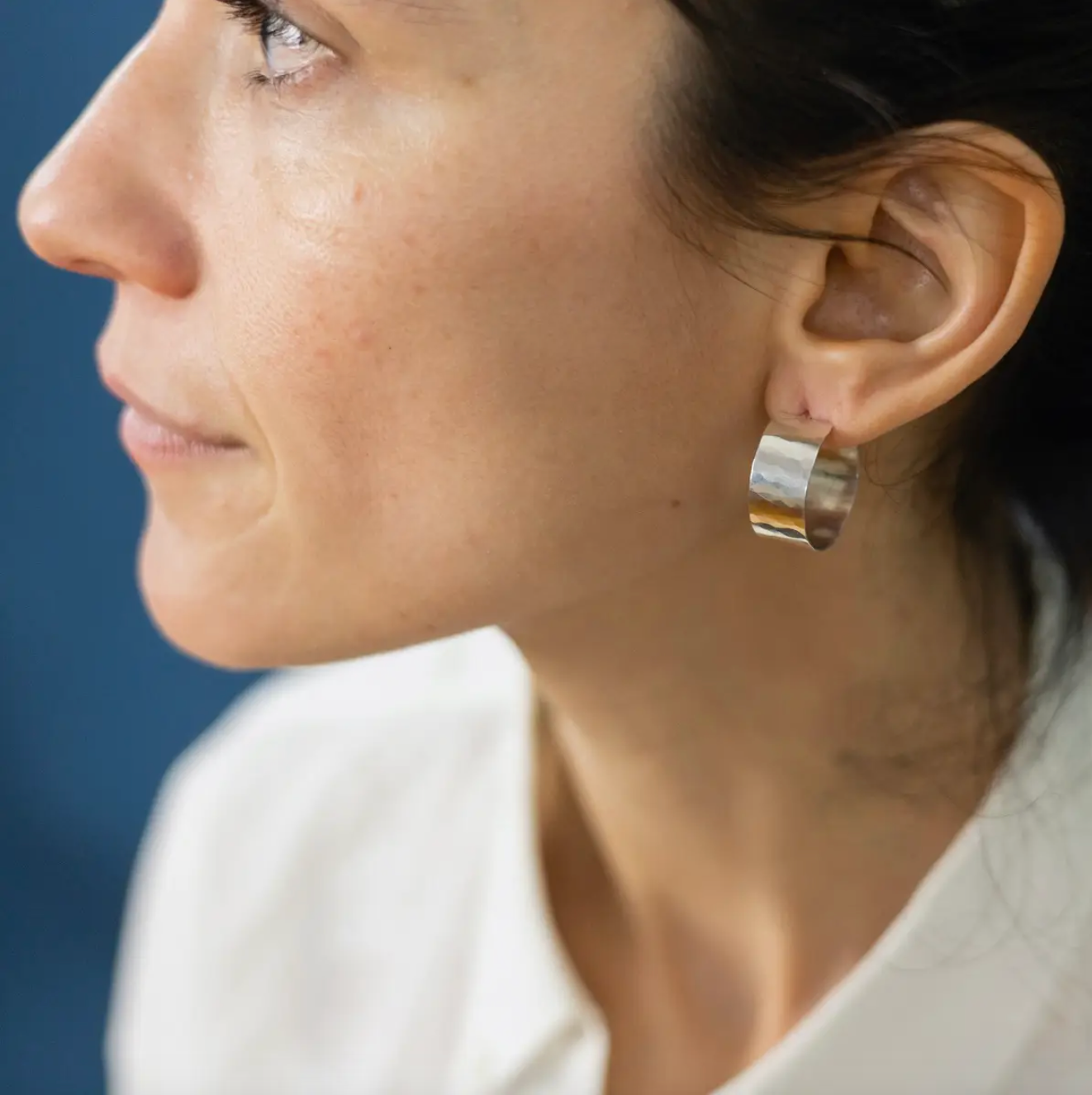 Side view of woman wearing small, flat hammered gold hoop earrings.