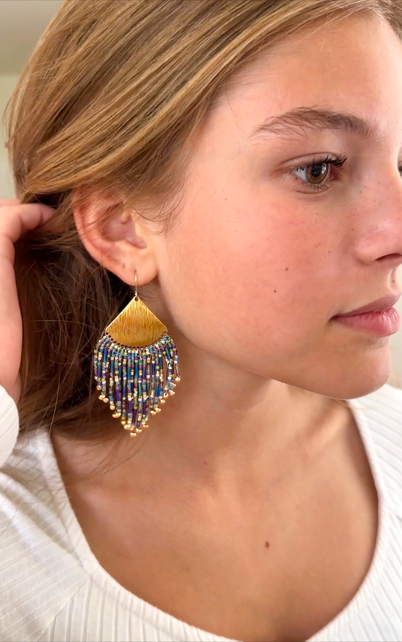 Woman wearing gold beaded fringe earrings with multi colored beads.