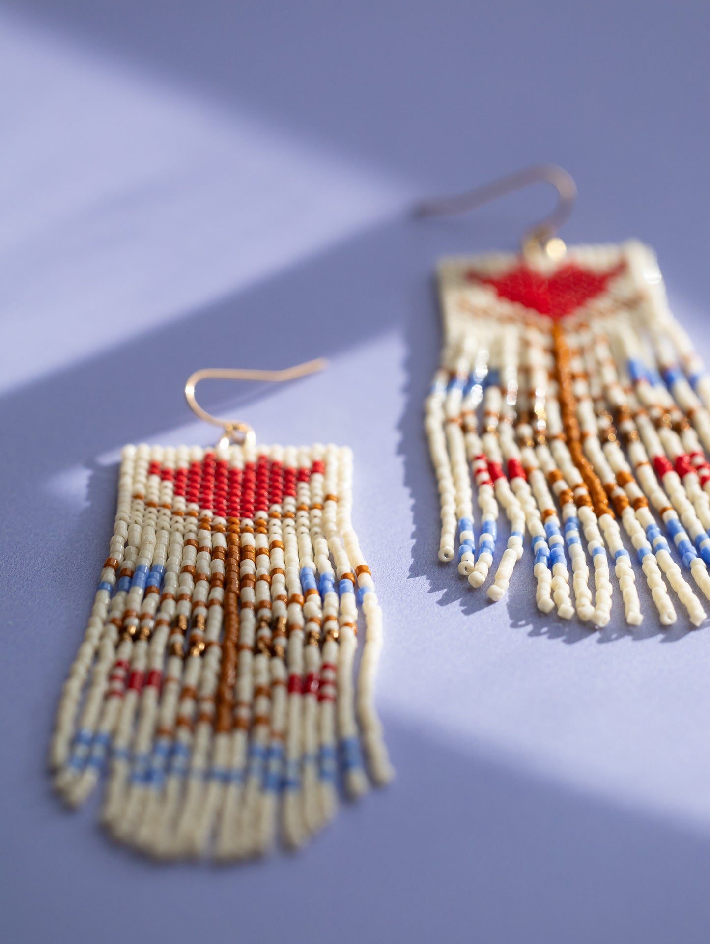 Hand beaded cream colored fringe earrings with red and blue vintage flower motif, close up.