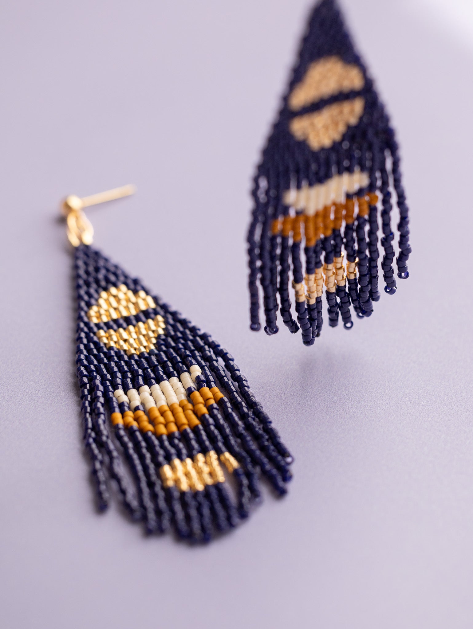 Navy hand beaded fringe earrings with gold half moon accents, one being held up and one laying flat.