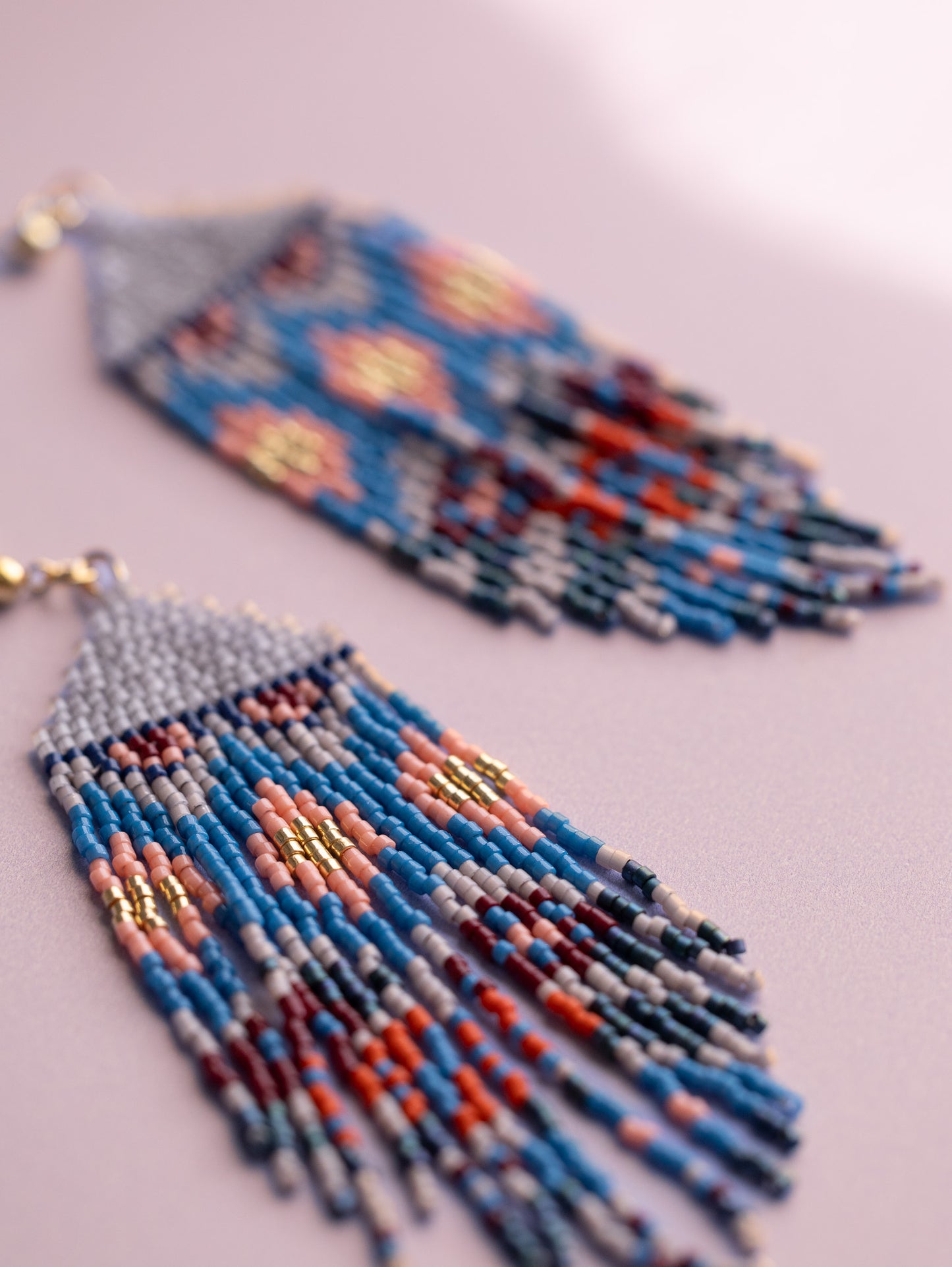 Handwoven beaded stud earrings with blue, pink, gold, red and gray colored beads, close up.