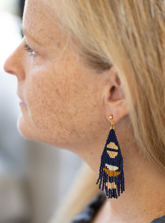 Woman wearing navy hand beaded fringe earrings with gold half moon accents.