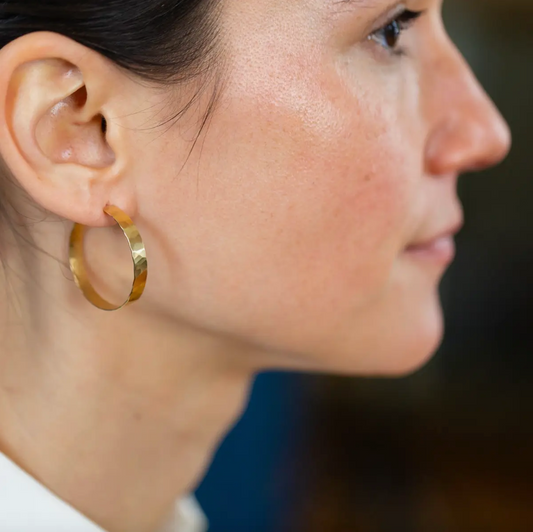 Woman wearing large thin gold hammered hoops.