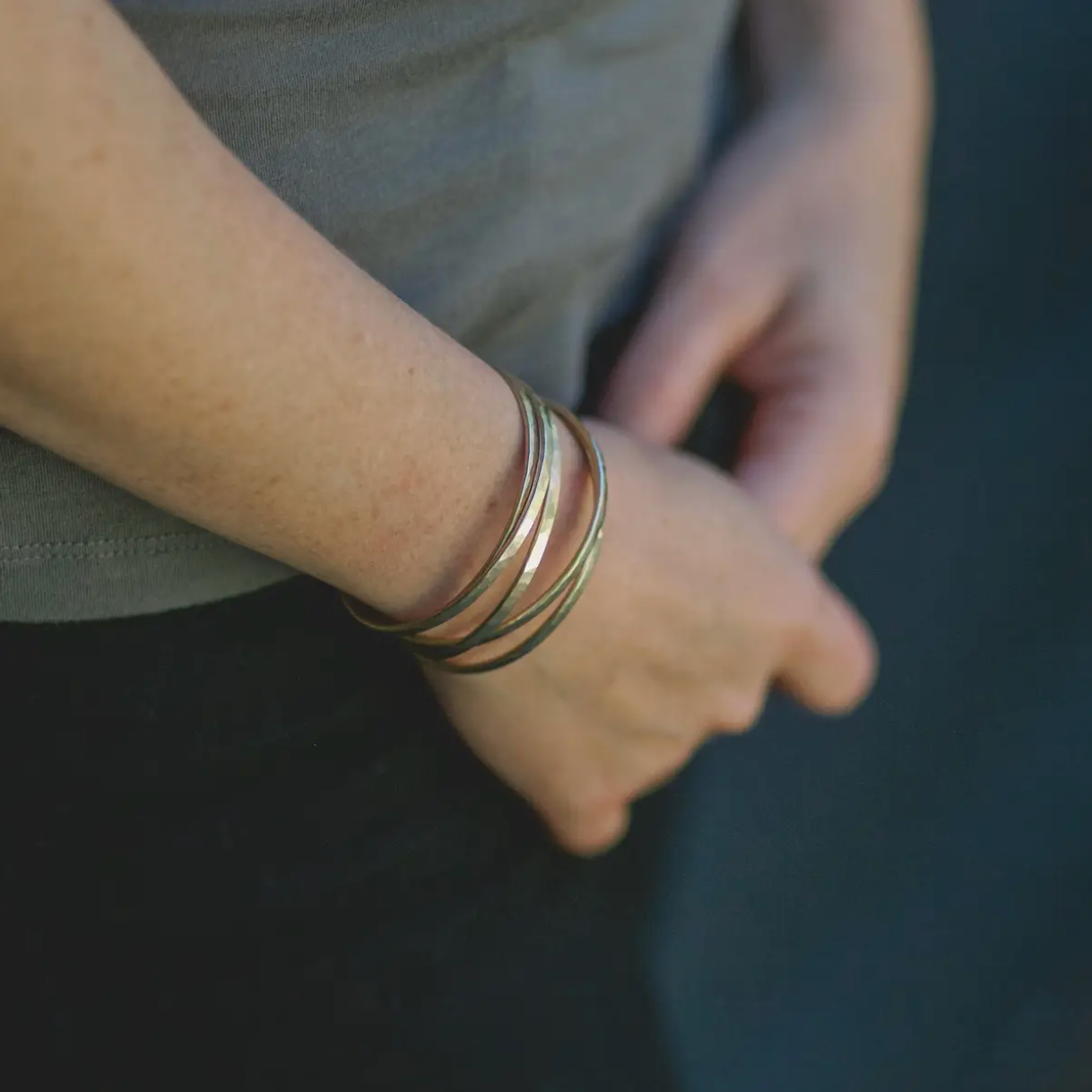 Person wearing several thin hammered brass cuff bracelets.