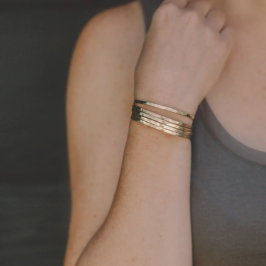 Woman wearing several thin hammered brass cuff bracelets.