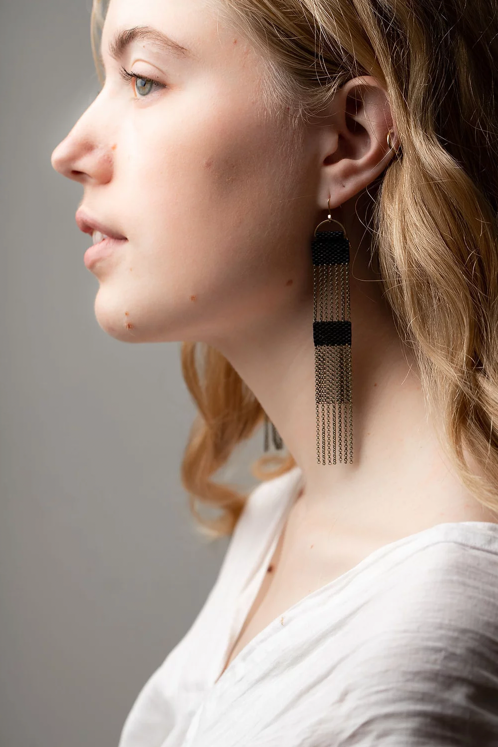 Woman wearing long dangle earrings made from black beads and brass chains.