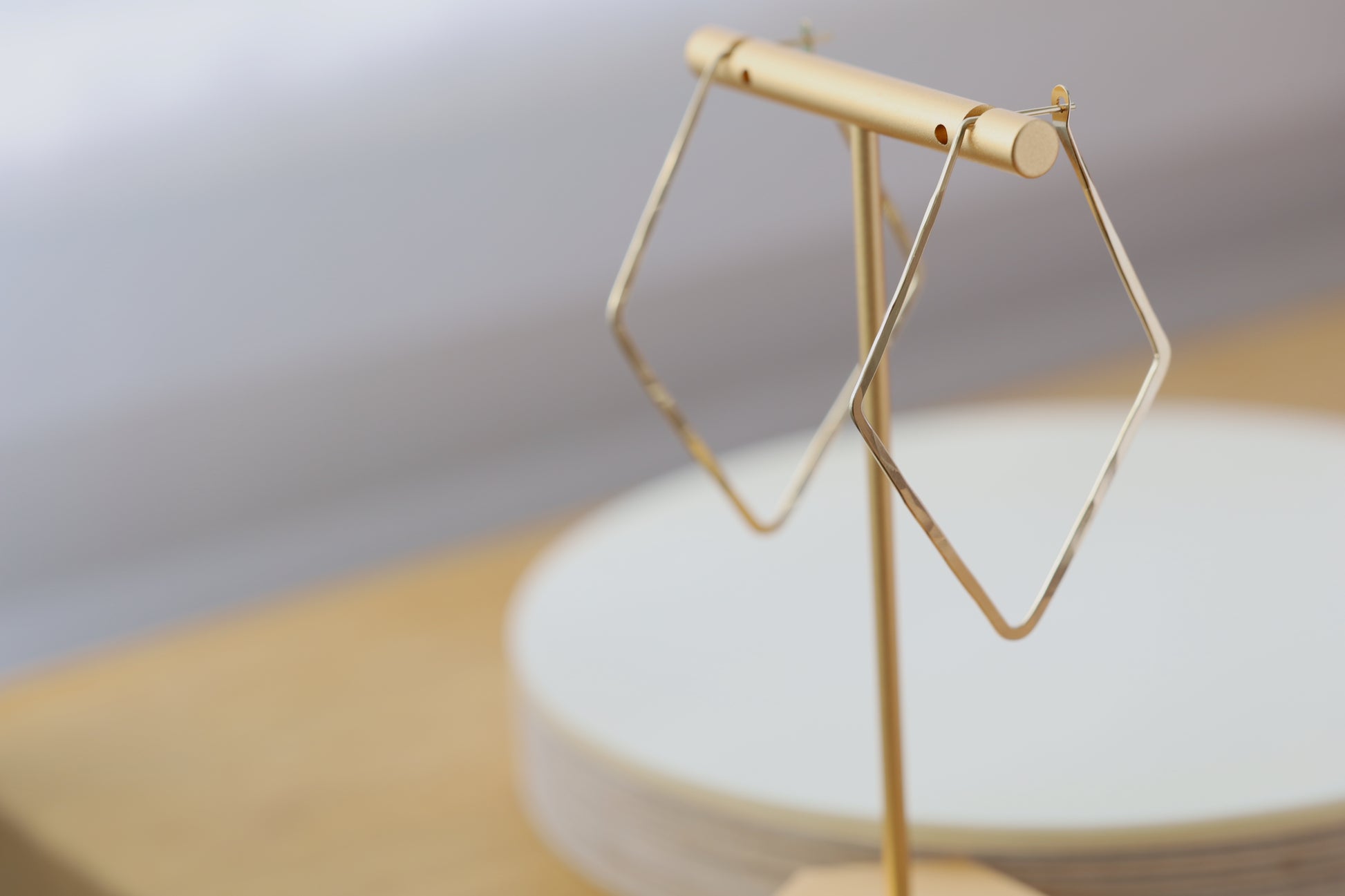 Diamond shaped hoop earrings in gold, hanging from an earring display.