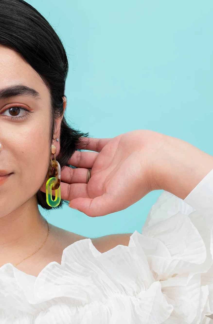 Woman wearing tortoise shell and florescent green acrylic link earrings.