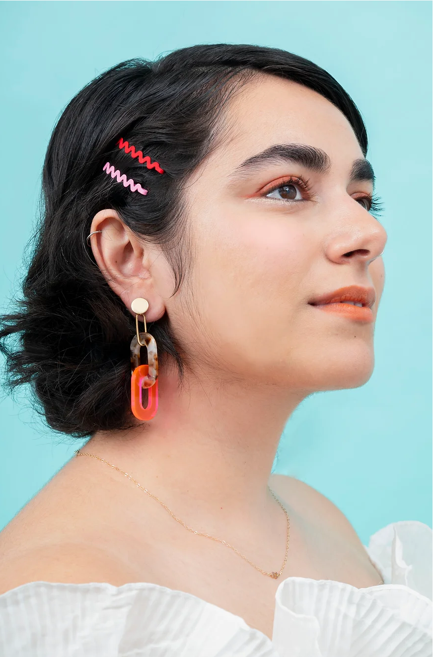 Woman wearing tortoise shell and florescent pink acrylic link earrings.