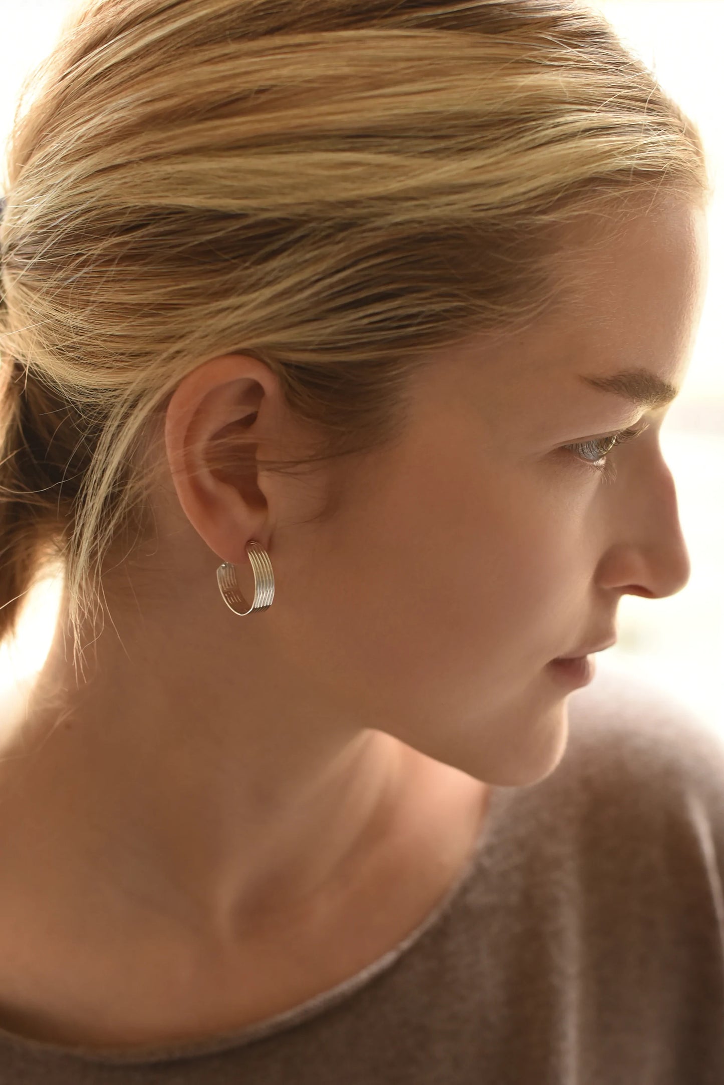 Woman wearing silver hoop earrings with linear designs, side view.