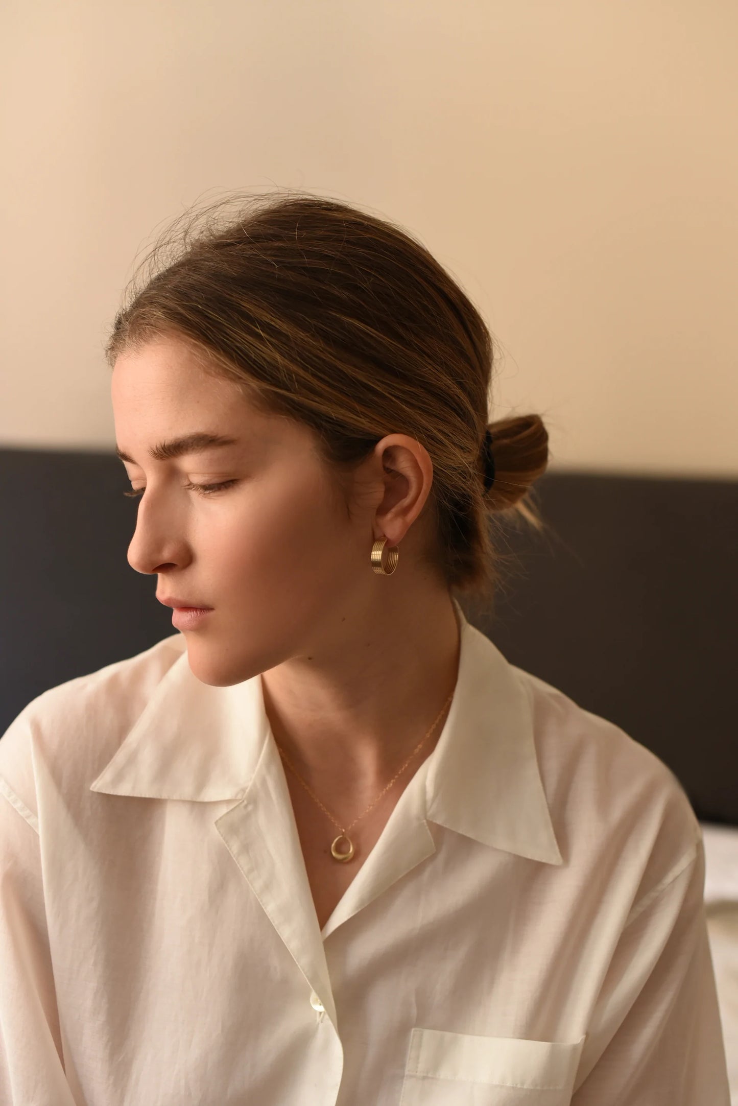 Woman wearing gold hoop earrings with linear designs, far away.