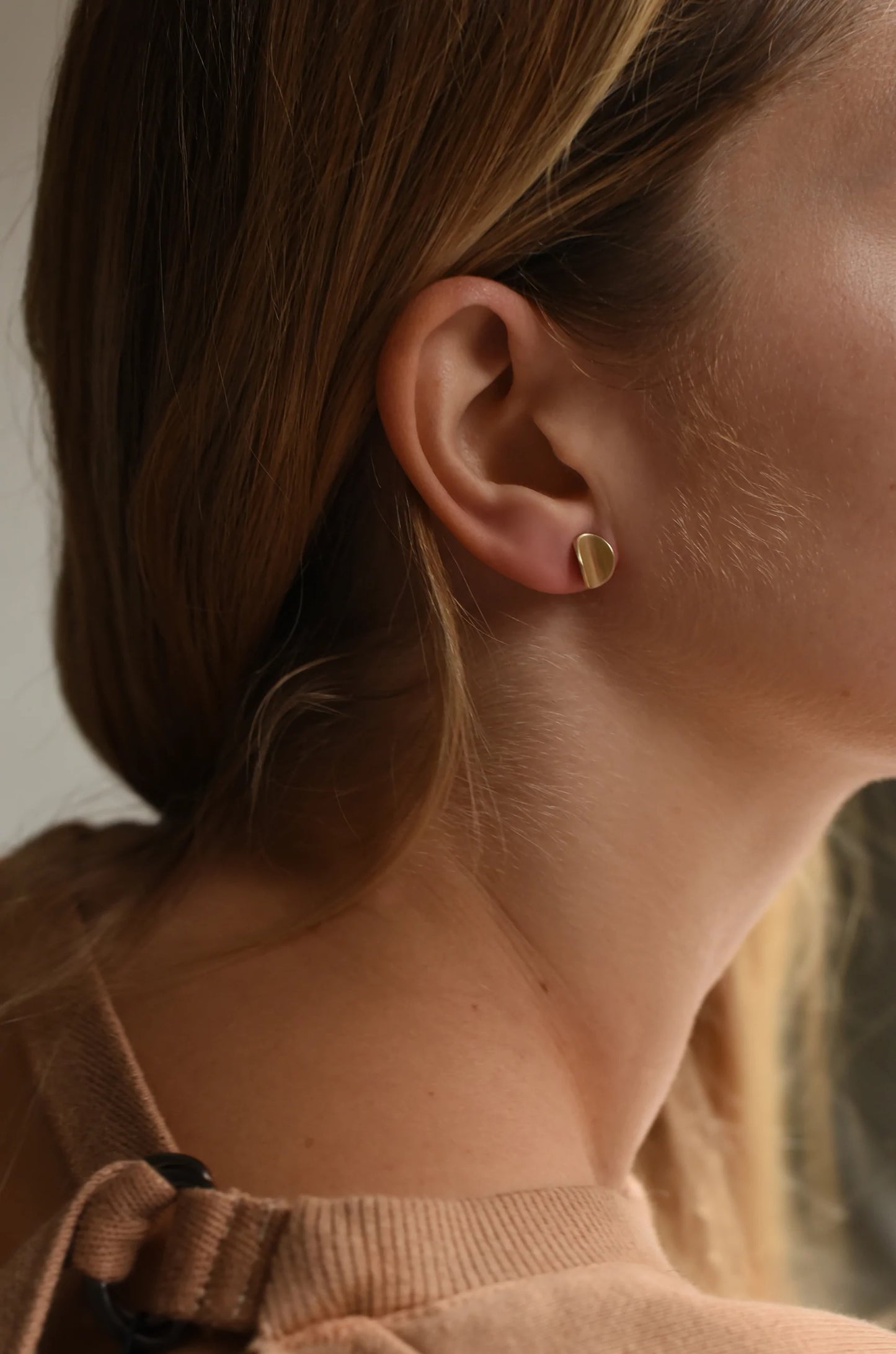Woman wearing curved organic shaped gold earring studs.