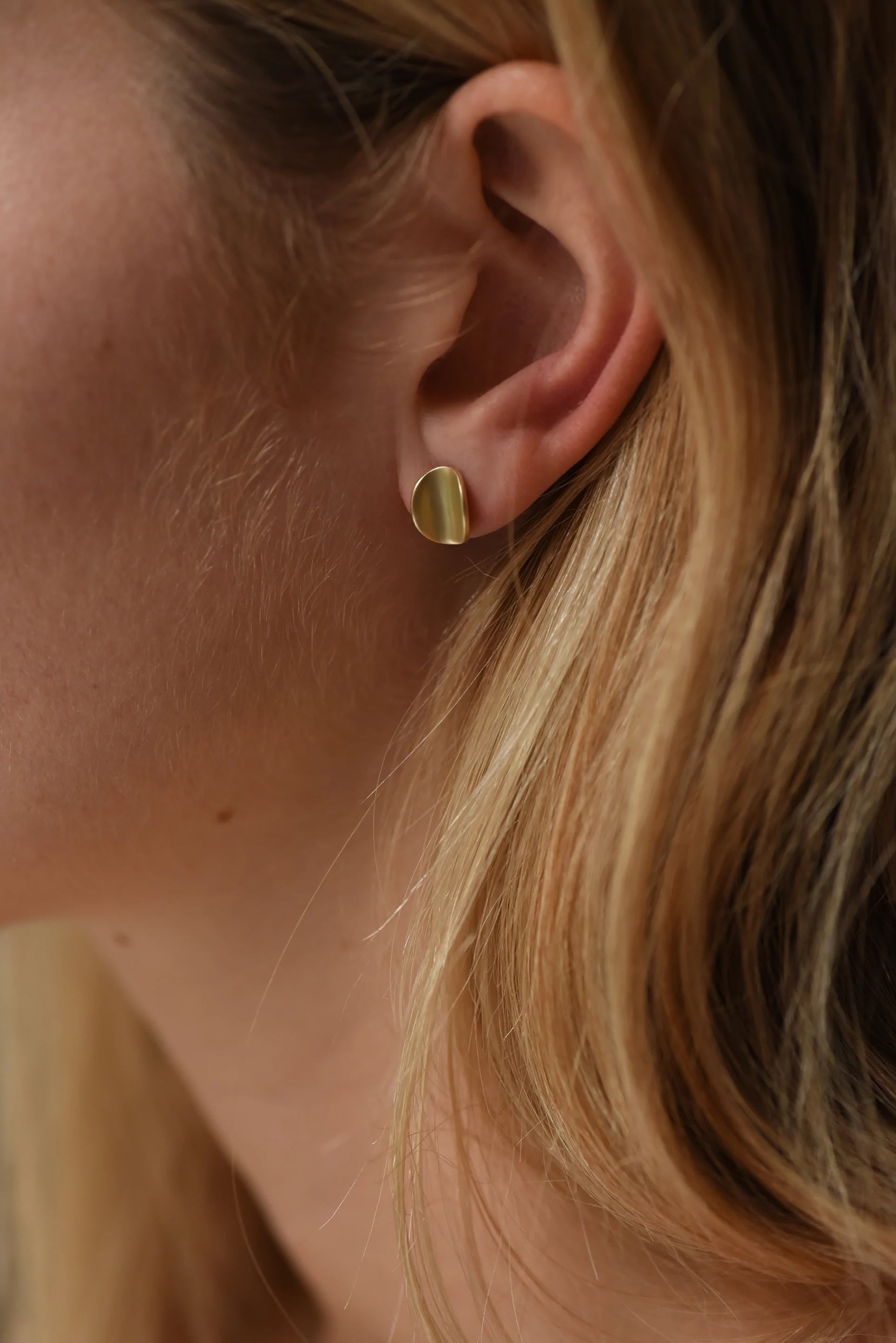 Woman wearing curved organic shaped gold earring studs.