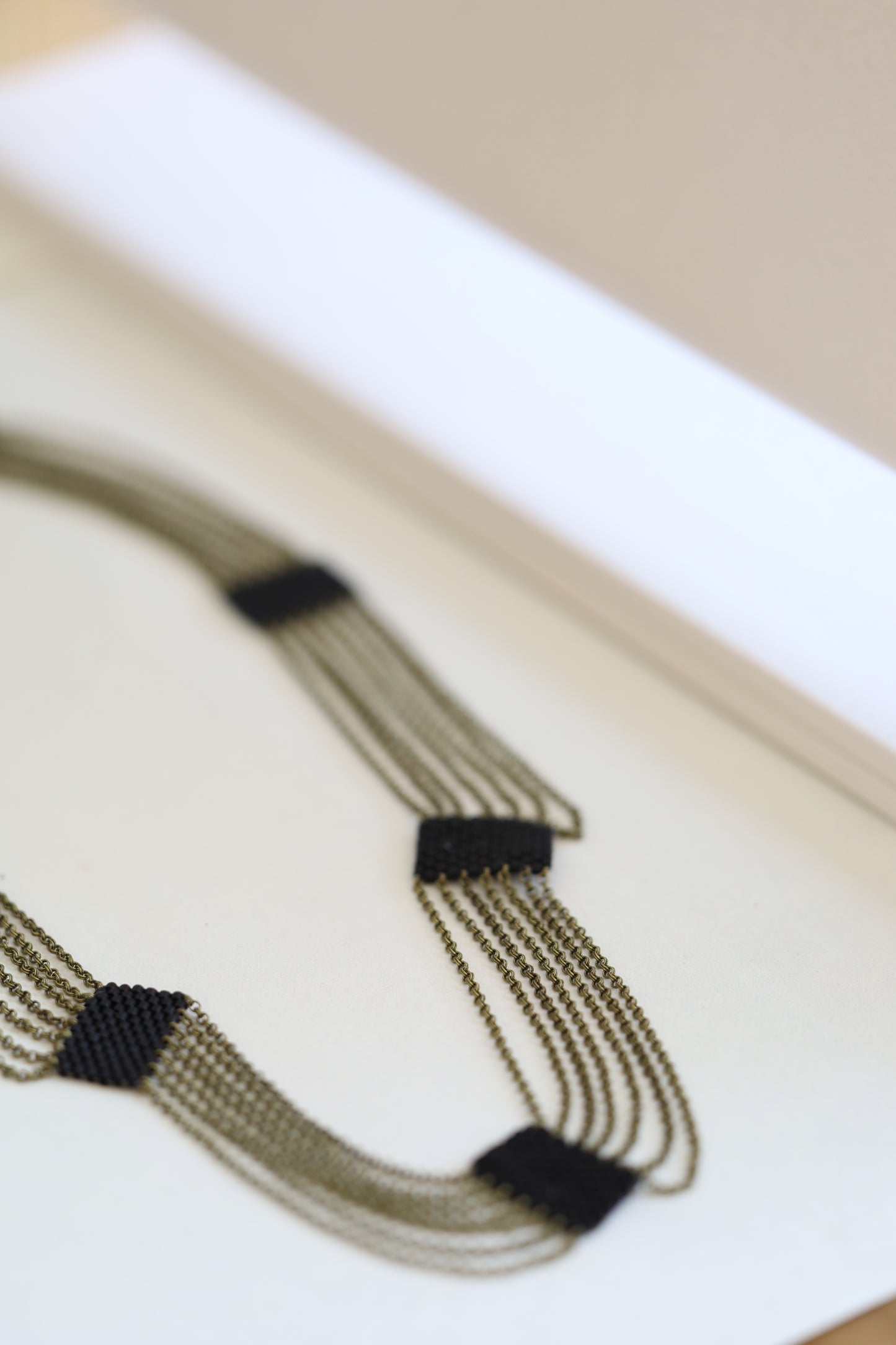 Elegant draping necklace made of chain and black beads laying on white background..