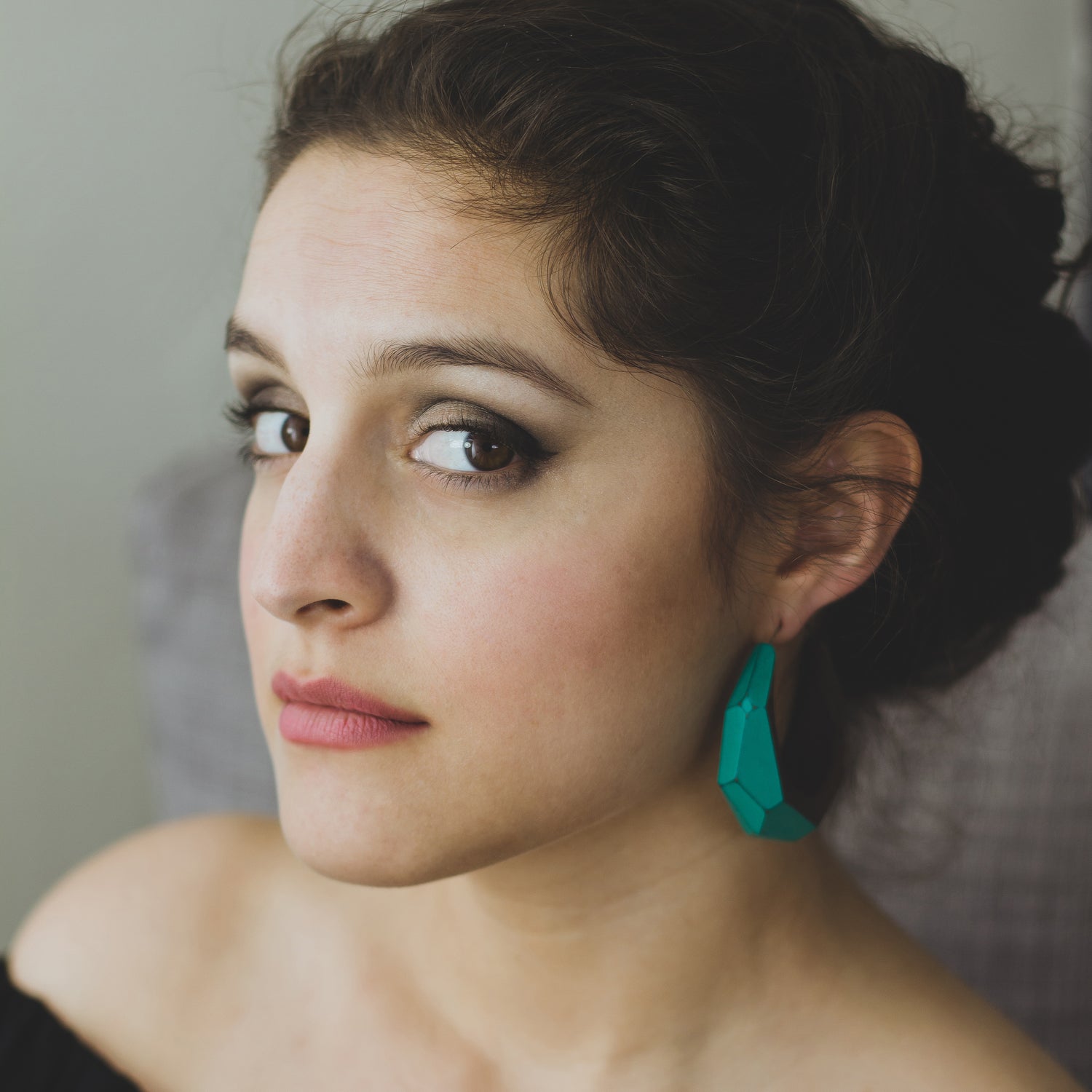 Woman wearing large statement hoop earrings made from wood with turquoise painted accents.