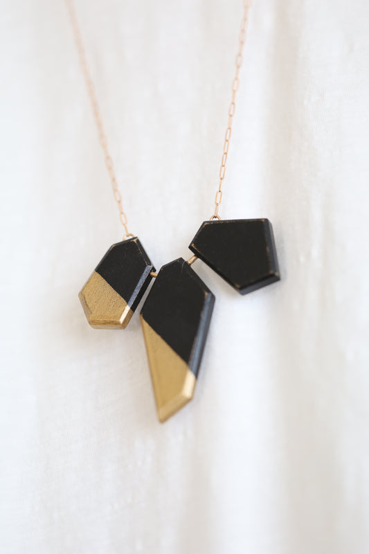 Wooden pieces painted black and gold on a bronze chain. Angled view.