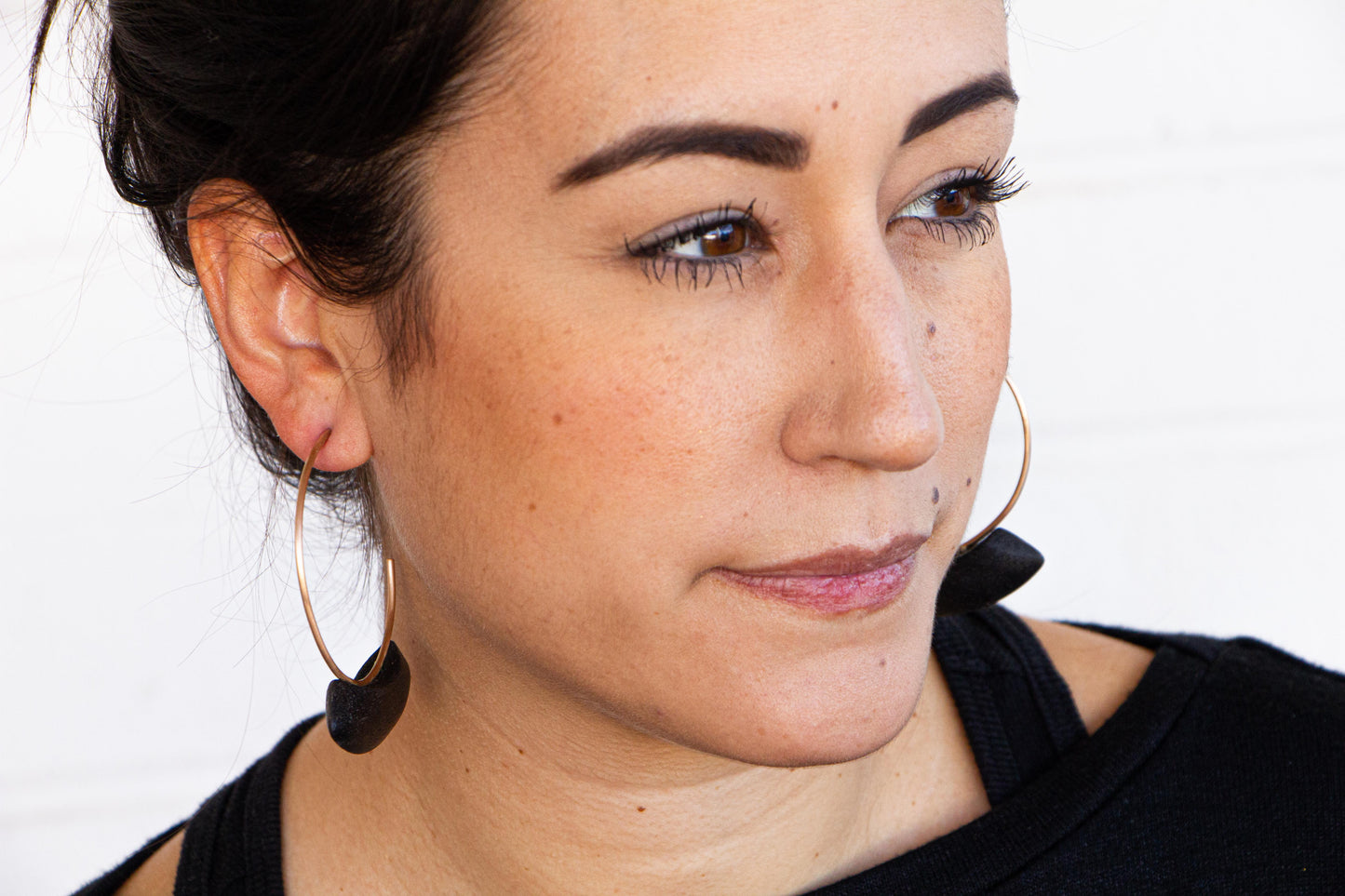 Woman wearing bronze and burnt wood hoop earrings.