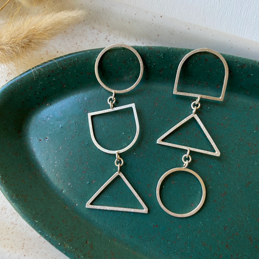 Pair of earrings made of geometric shapes in a green dish.