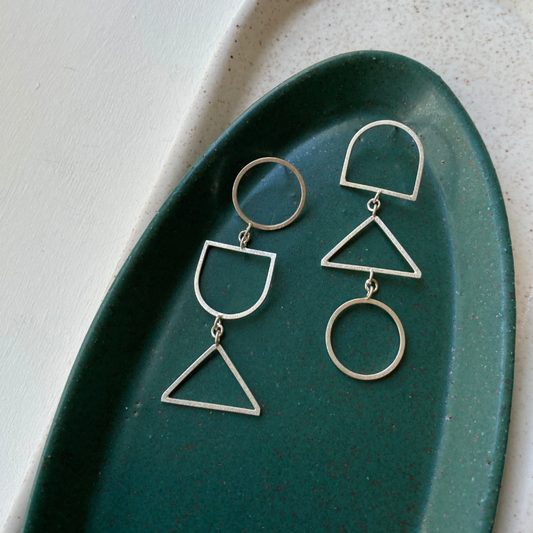 Pair of long earrings made of geometric shapes in a green dish.