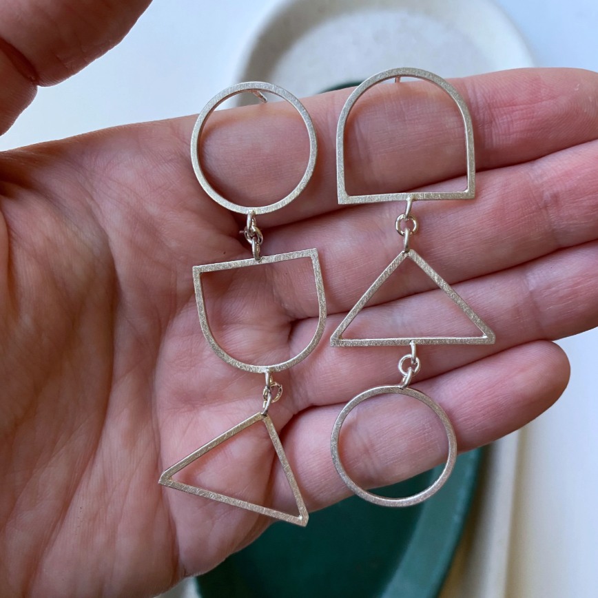 Pair of earrings made of geometric shapes being held against a hand.