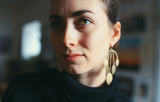 Woman wearing large gold statement earrings made from leaf shapes.